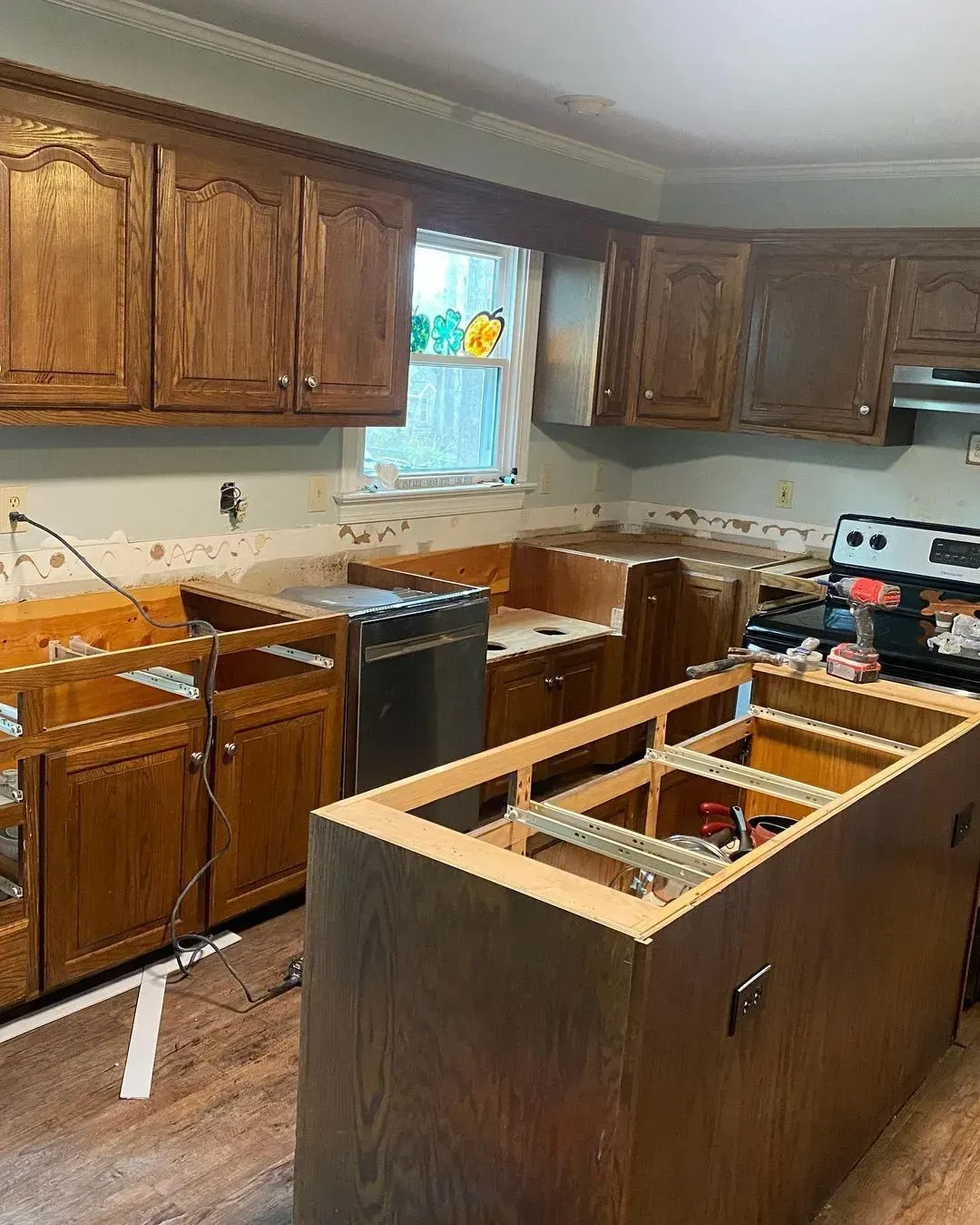 Kitchen under renovation with dark wood cabinets, removed island panels, and tools on the countertop.