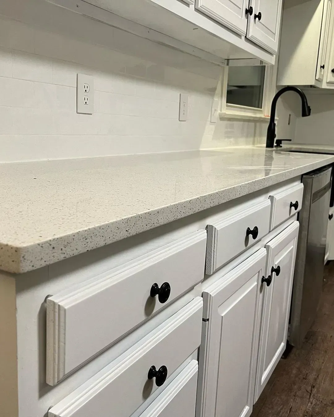 White kitchen countertop with white cabinets and black knobs, viewed along the counter