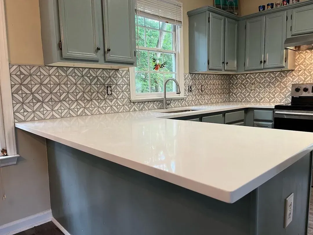 Modern kitchen with white island, gray cabinets, patterned backsplash, and a window above the sink