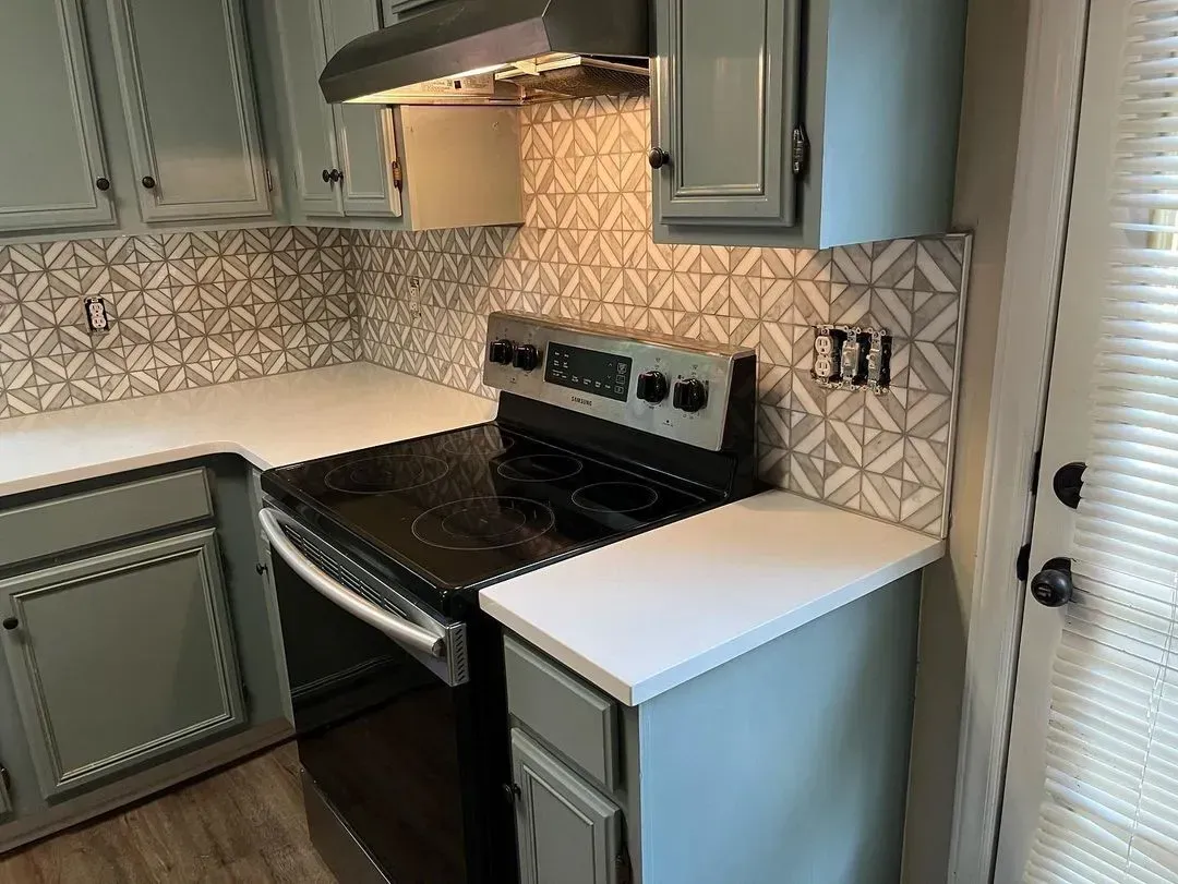 Modern kitchen with gray cabinets, white countertops, black stove, and patterned backsplash
