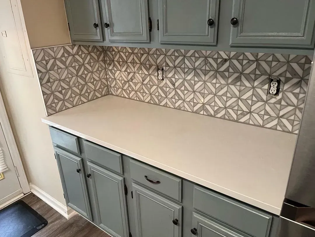 Kitchen countertop and cabinets with gray doors and a geometric tile backsplash in a bright room
