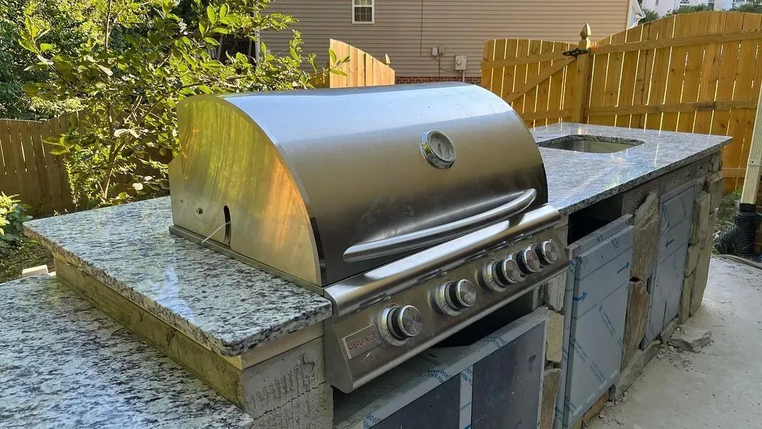 Stainless steel gas grill built into an outdoor stone countertop in a backyard