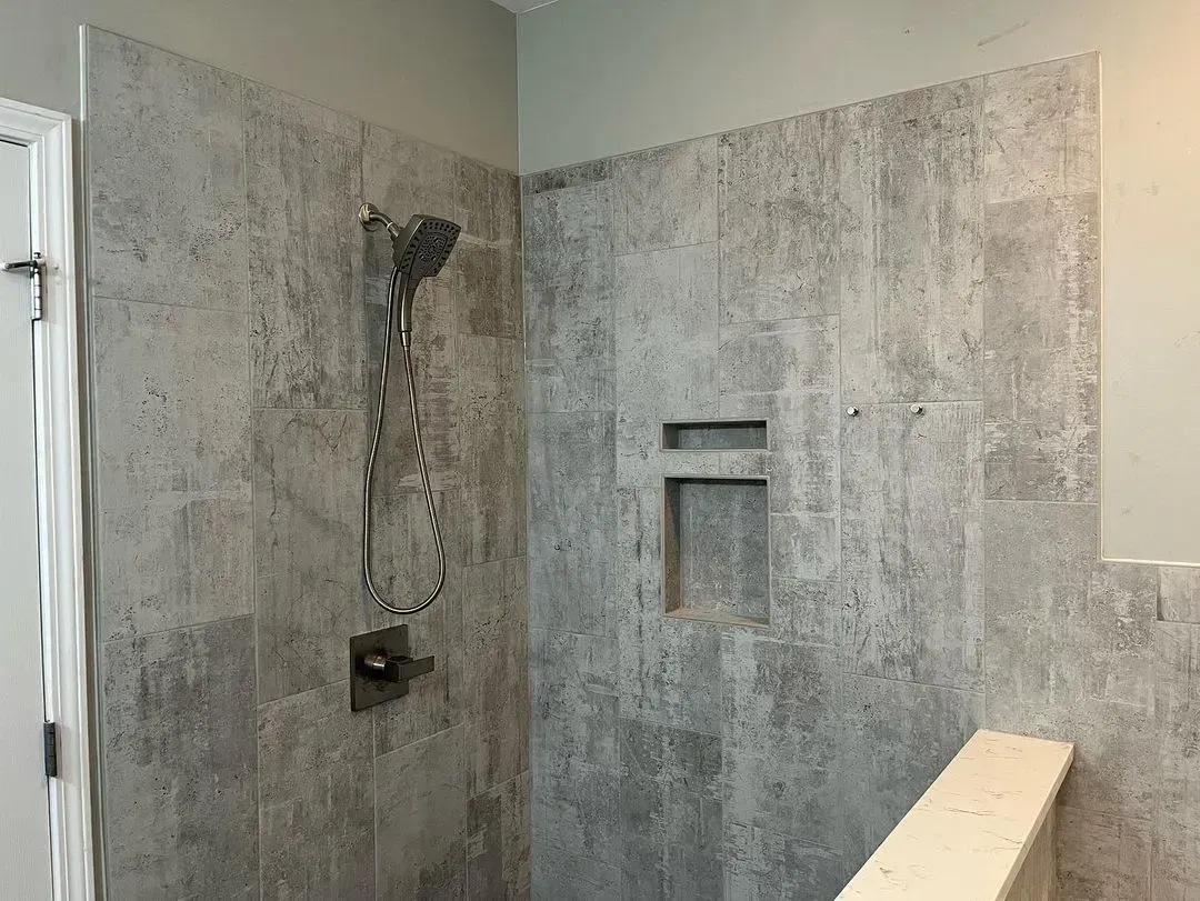 Bare concrete shower stall with exposed plumbing and a wooden bench seat