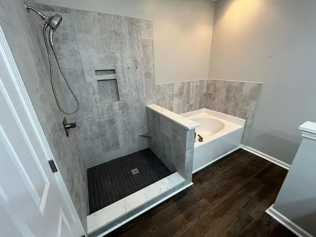 Accessible bathroom with roll-in shower, grab bar, and bathtub beside dark wood flooring
