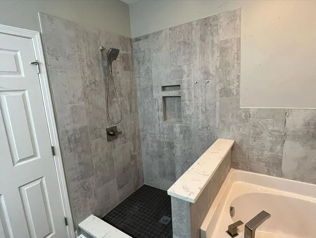Bathroom with tiled shower area, glassless tub, and gray walls under renovation
