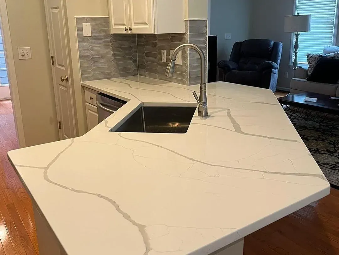 Modern kitchen with white marble island countertop and black sink opening, damaged with visible cracks.