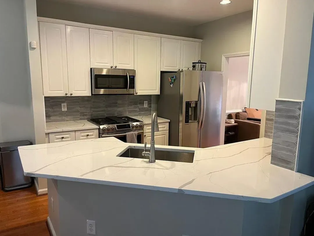 Modern kitchen with white cabinets, stainless steel appliances, and a white island with a sink.