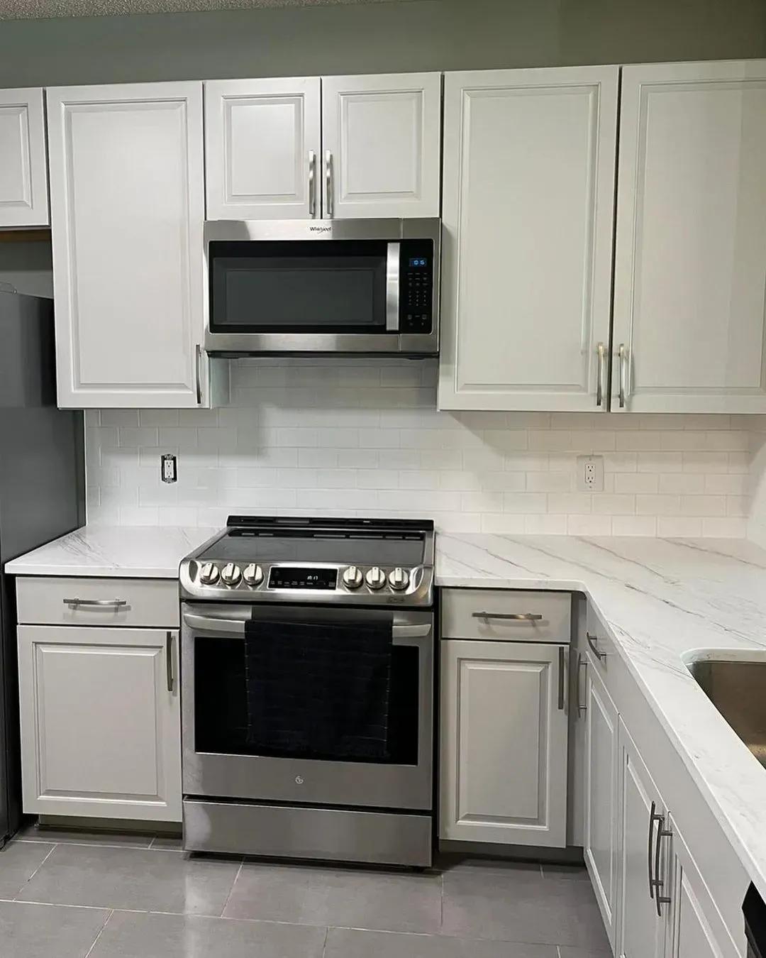 Modern white kitchen with stainless steel stove and microwave, white cabinets, and light countertops.