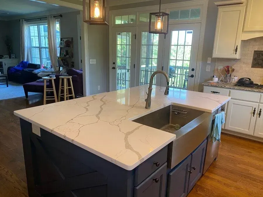 Modern kitchen with large marble island, sink, pendant lights, and French doors to a patio.