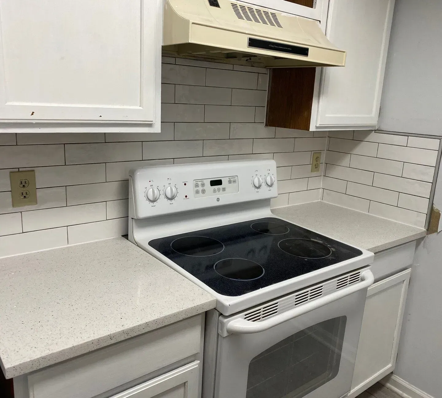 Modern kitchen with white cabinets, white subway tile, and a white electric stove under a vent hood