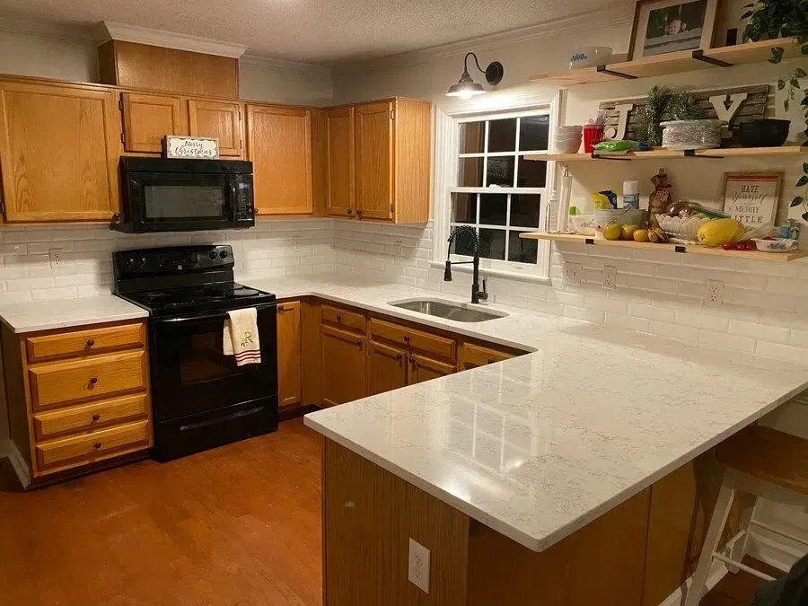 Kitchen interior with wooden cabinets, black appliances, white countertops, and a window over the sink.