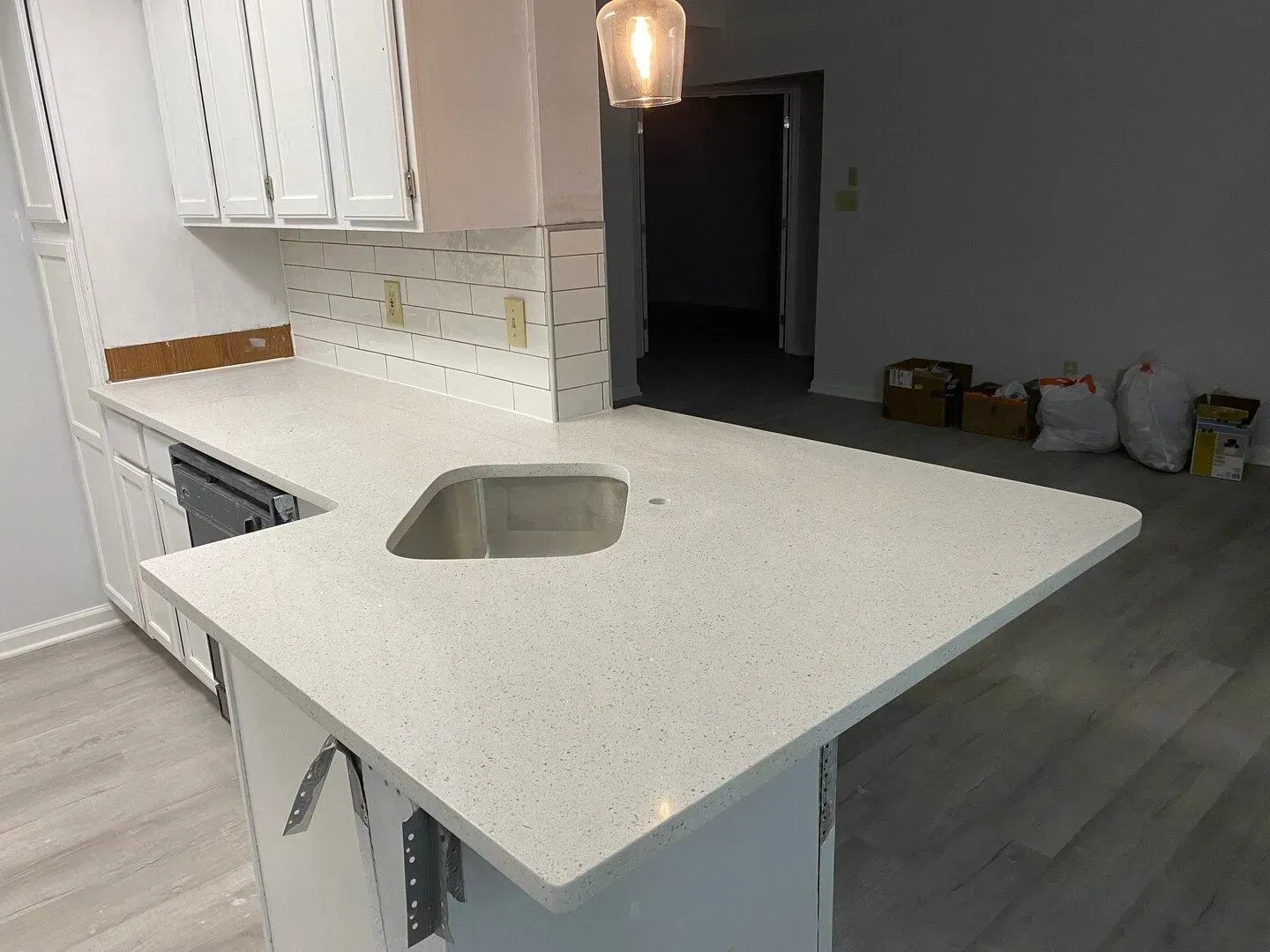 Modern kitchen with white cabinets, quartz island, and stainless sink in a gray-floored open space