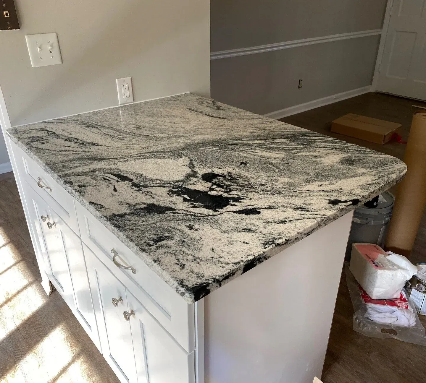 White kitchen island cabinet with black-and-white granite countertop in a partially renovated room