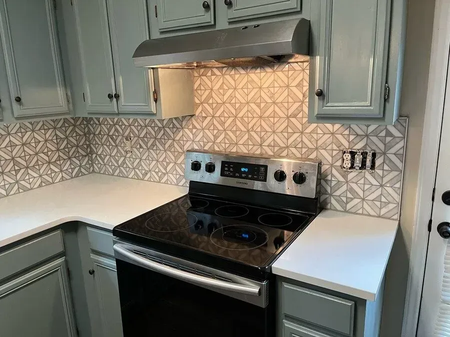 Kitchen stove with stainless range, white cabinets, and patterned tile backsplash under a vent hood