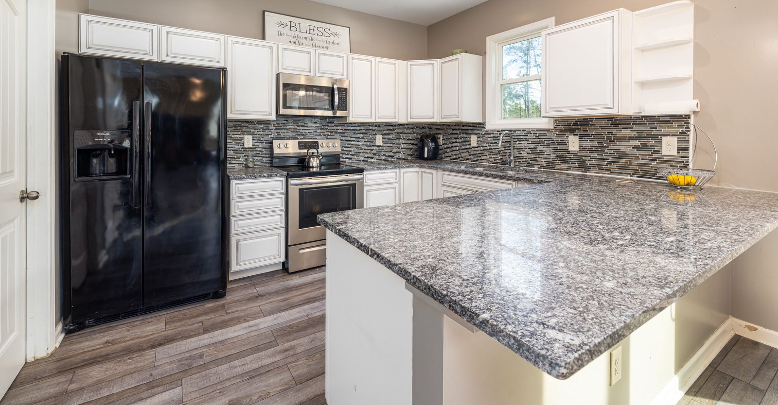 Modern kitchen with black appliances, white cabinets, and a granite island counter