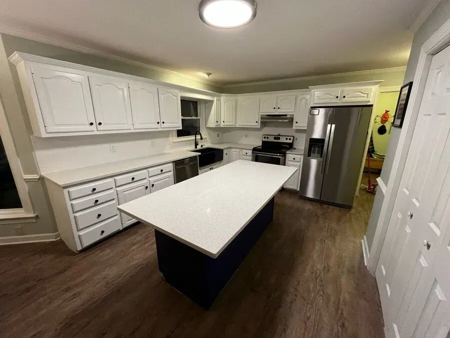 Bright white kitchen with island, stainless steel appliances, and dark wood flooring