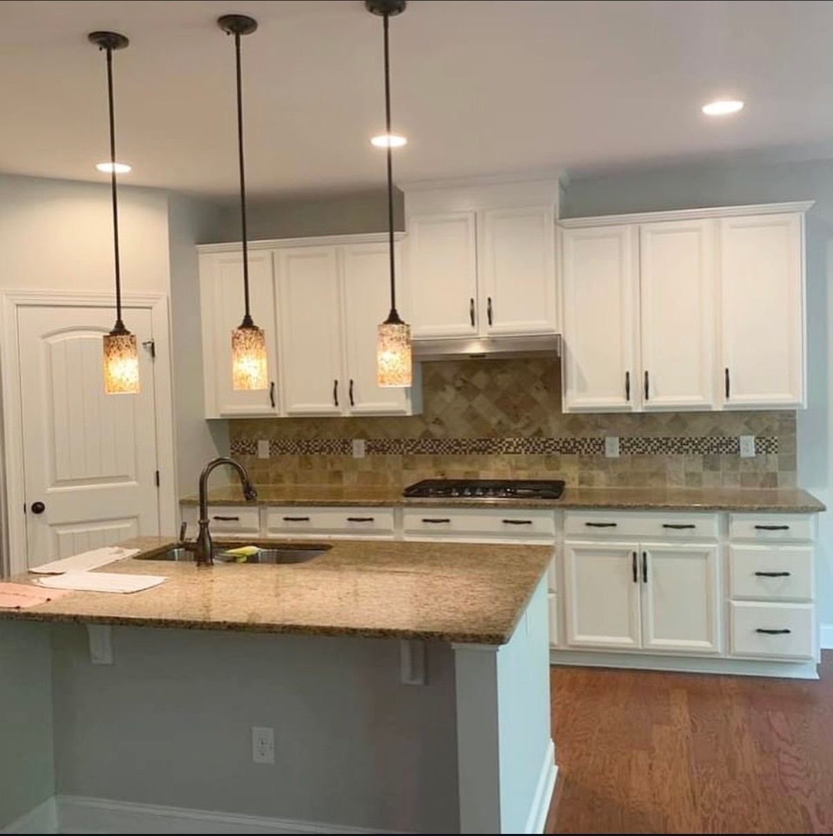 Bright modern kitchen with white cabinets, granite island, pendant lights, and stainless steel appliances
