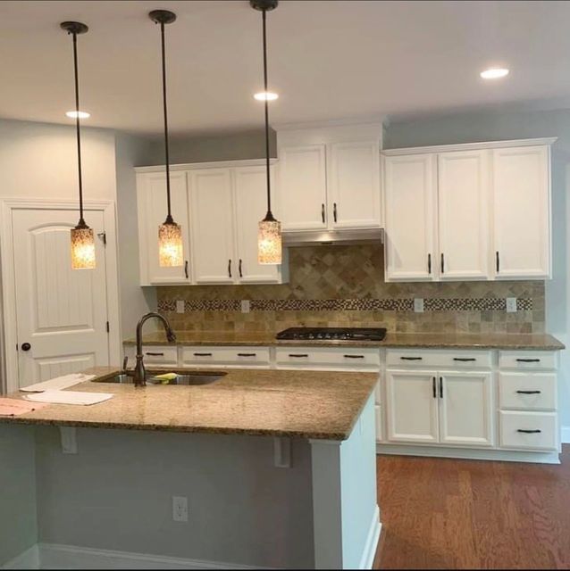 Bright modern kitchen with white cabinets, granite island, pendant lights, and stainless steel appliances