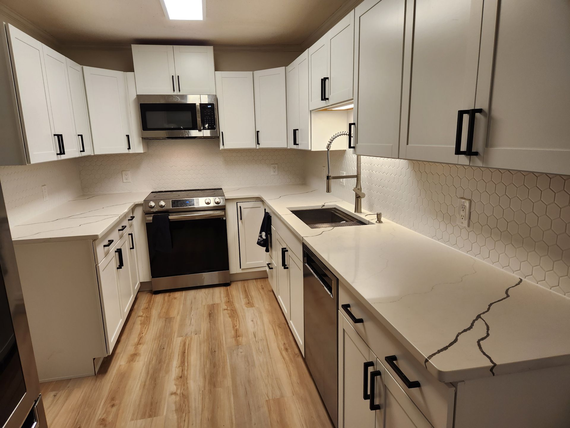 Bright white galley kitchen with black appliances and long speckled countertops