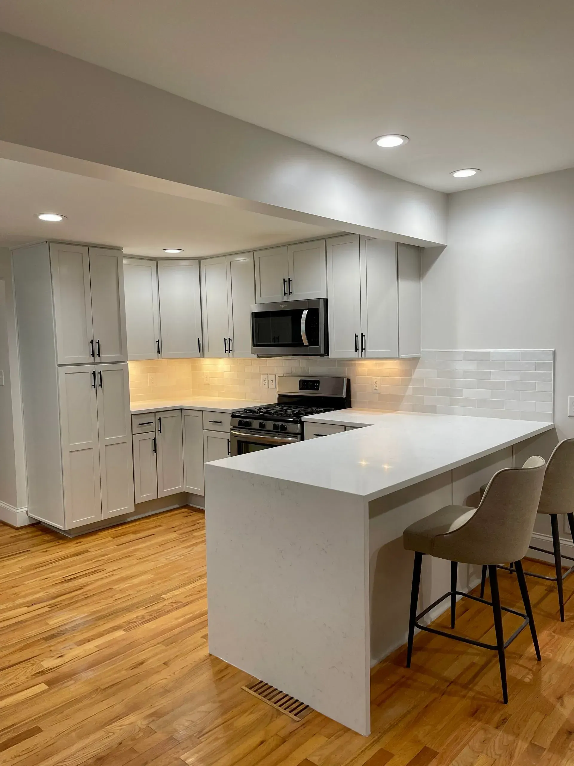 Modern white kitchen with island, stainless appliances, light wood floors, and two stools