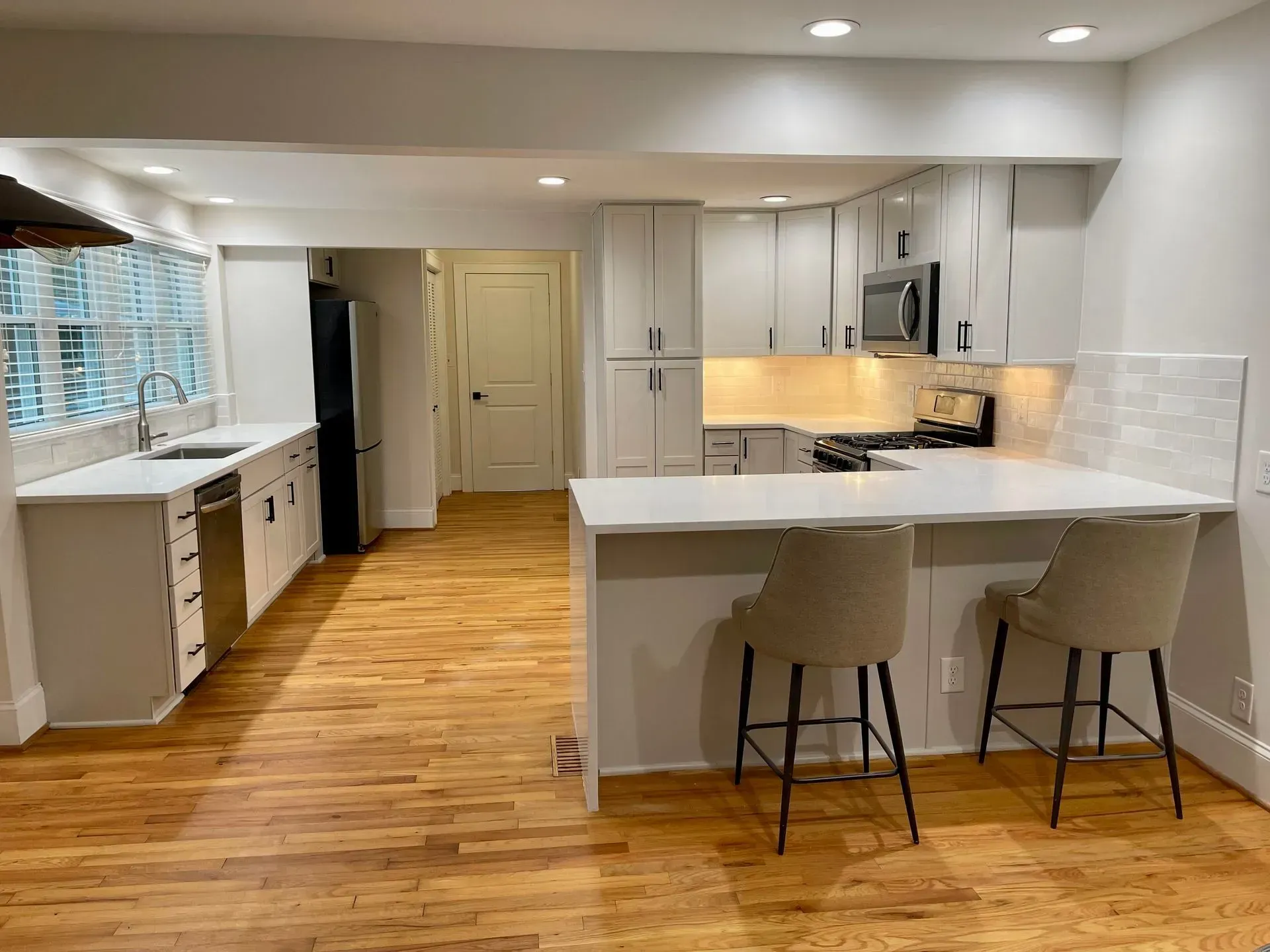 Bright white kitchen with island, bar stools, cabinets, and light wood floors in a modern open space