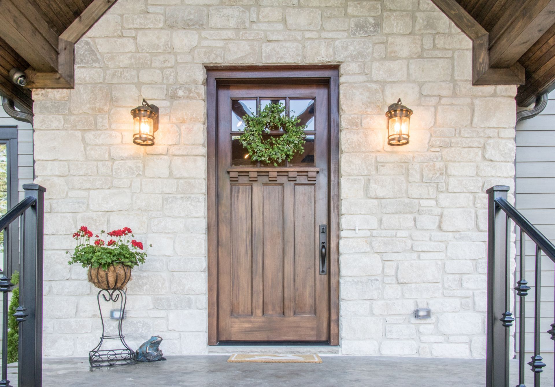 Stone house entry with wooden door, lanterns, and potted flowers on the porch