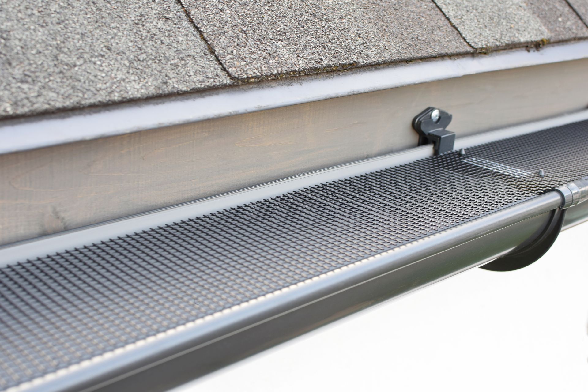Gutter guard under a shingled roof edge with a downspout connection