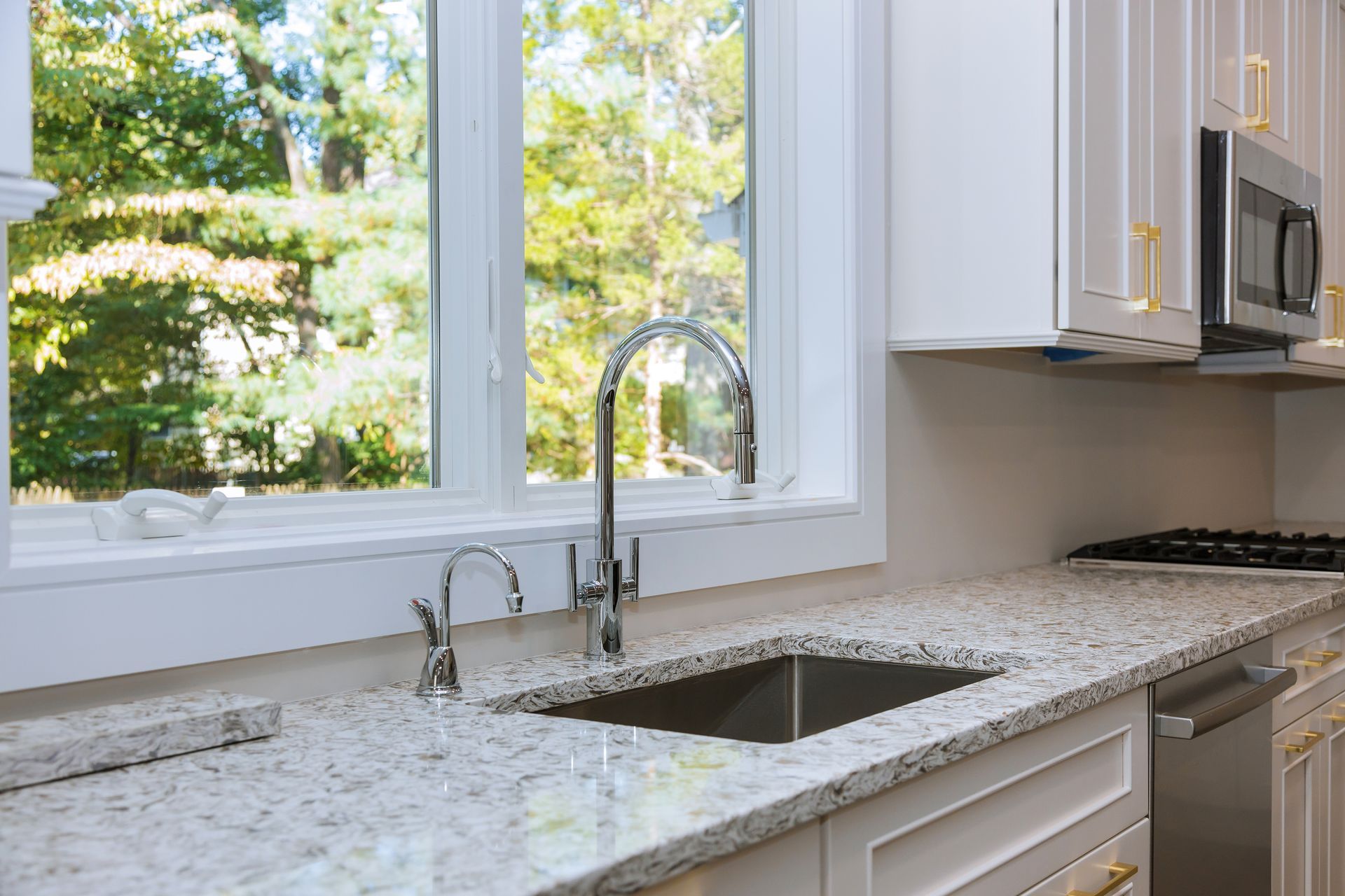 Bright modern kitchen with granite countertops, stainless sink, and a large window overlooking trees