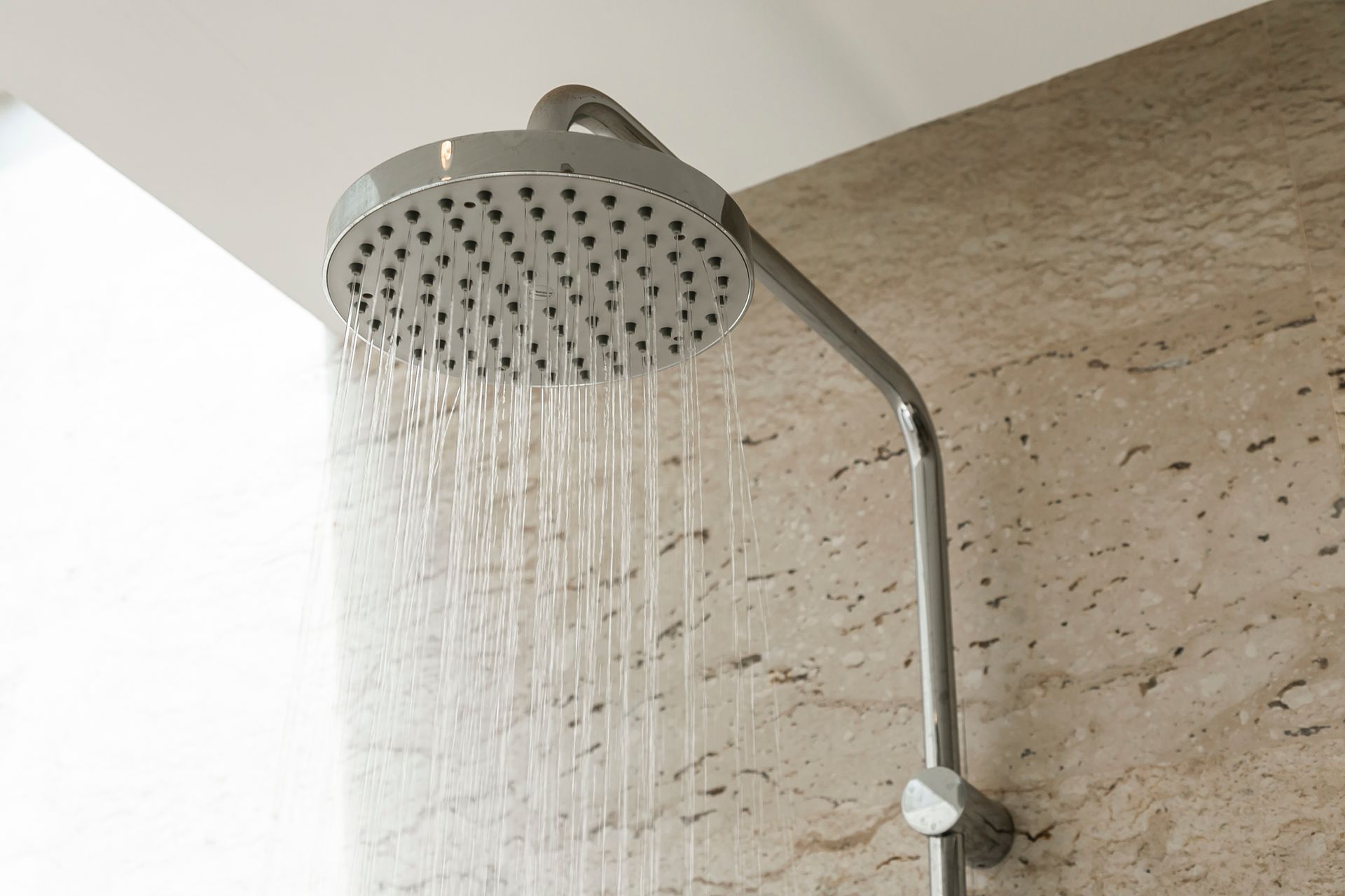 Modern showerhead running water against a beige tiled bathroom wall Modern showerhead running water against a beige tiled bathroom wall