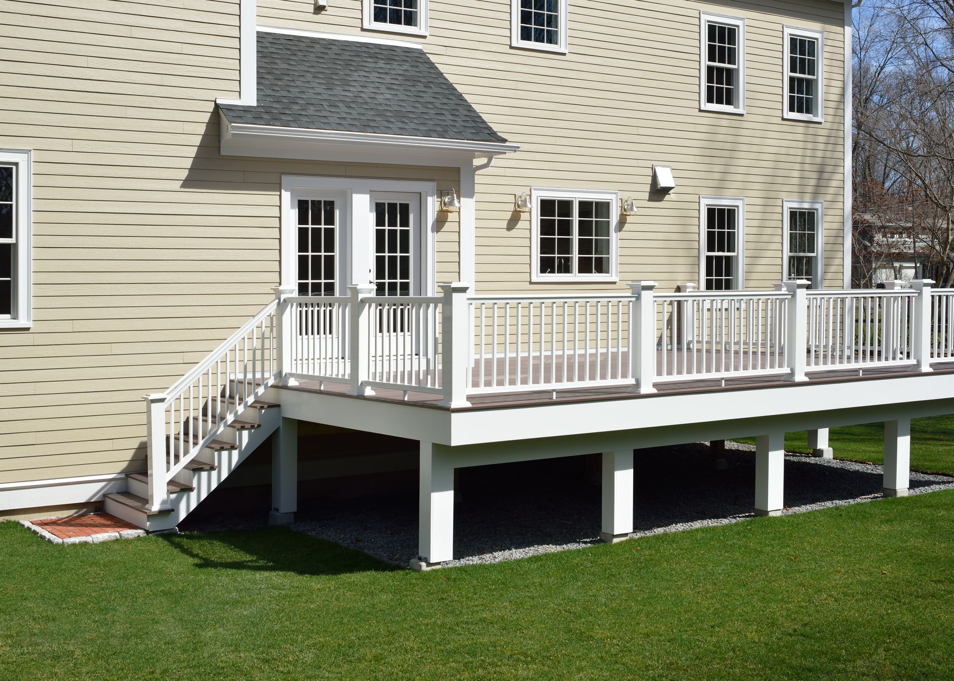 Wooden deck beside a modern house, with rocks in front and outdoor chairs near glass doors.