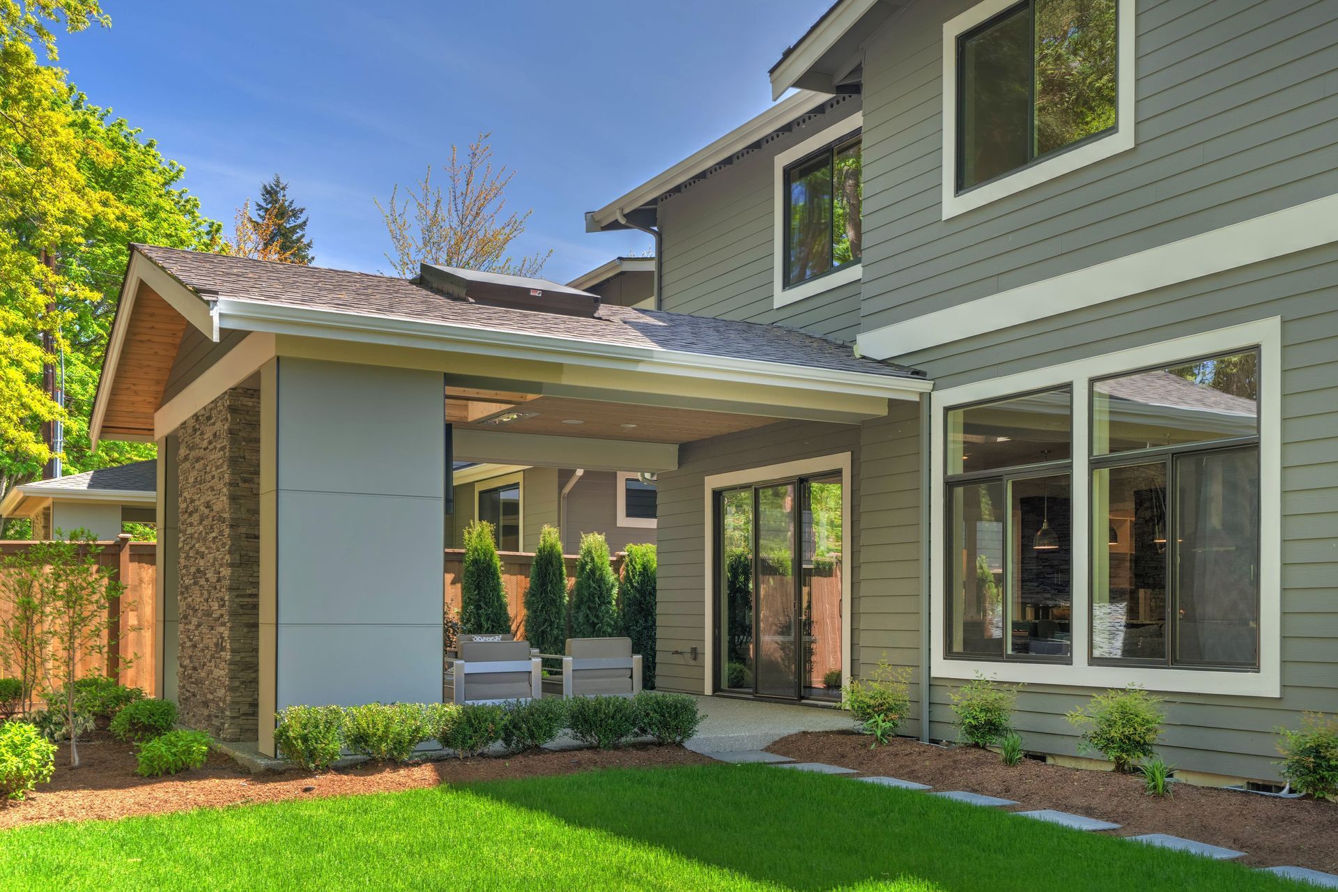 Modern two-story gray house with covered porch, large windows, and a green front lawn