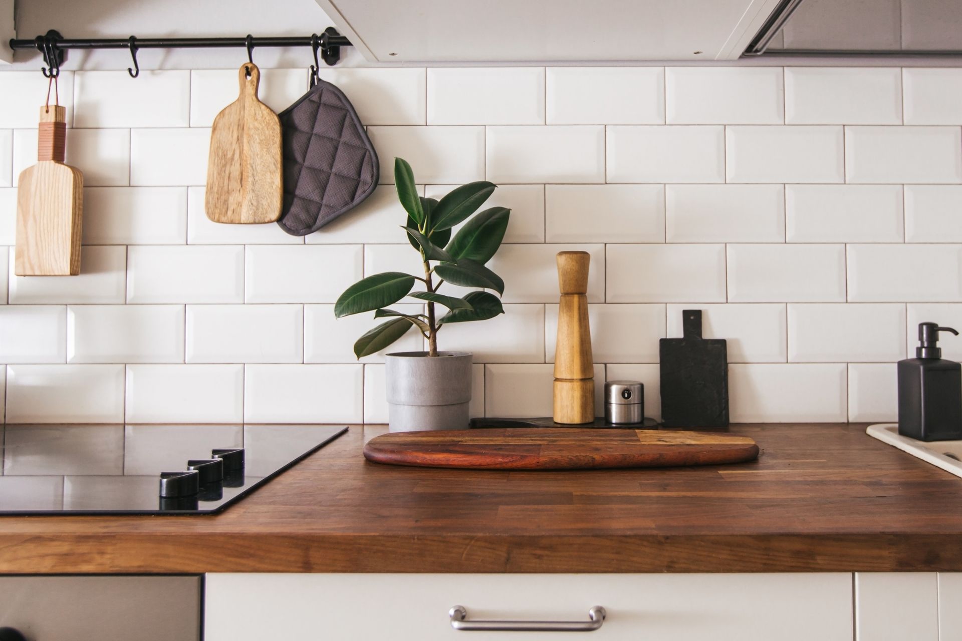 Modern kitchen counter with wooden cutting board, potted plant, utensils, and white subway tile backsplash