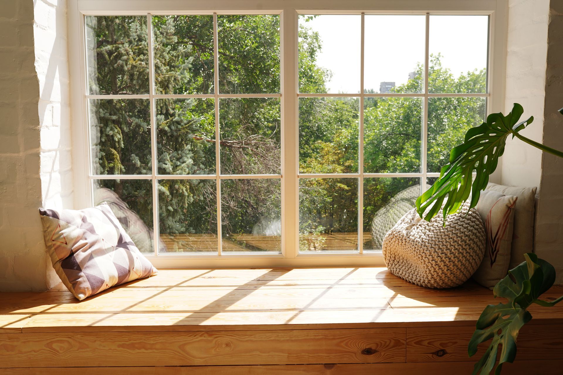 Sunlit window seat with cushions, a woven basket, and a potted plant overlooking greenery