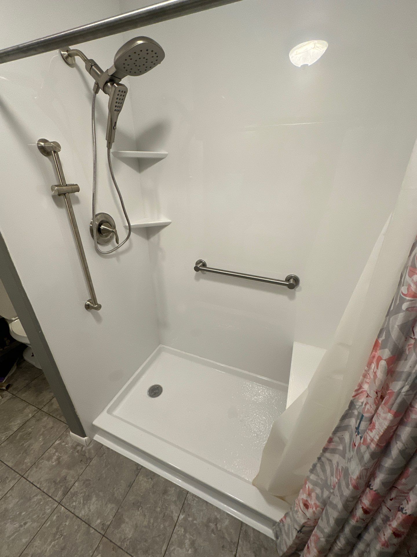 Accessible shower stall with grab bars, handheld showerhead, built-in shelves, and a shower curtain.