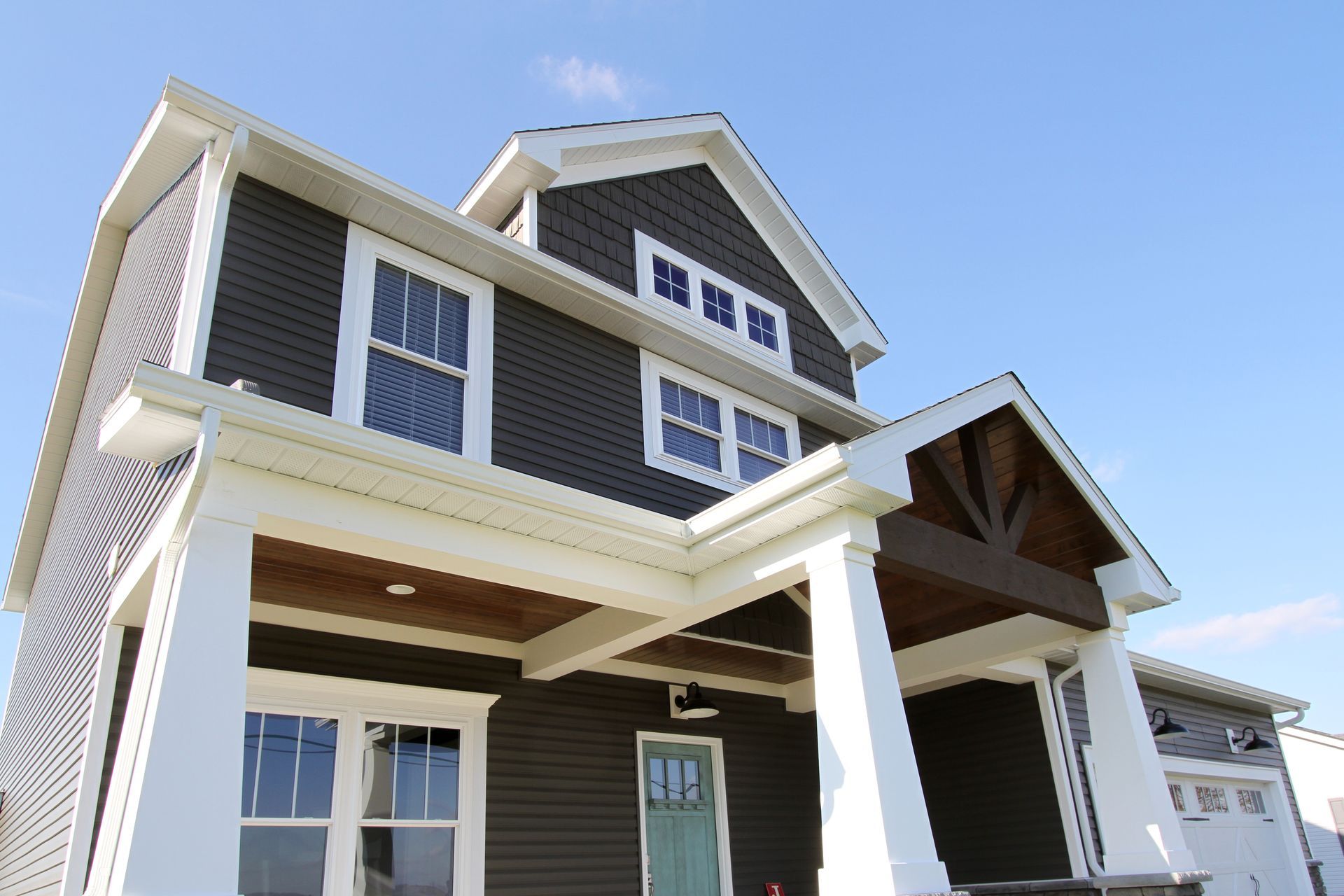 Man at a firm foundation construction booth with a branded table and banner display. Modern two-story house with dark siding, white trim, and a front porch against a blue sky
