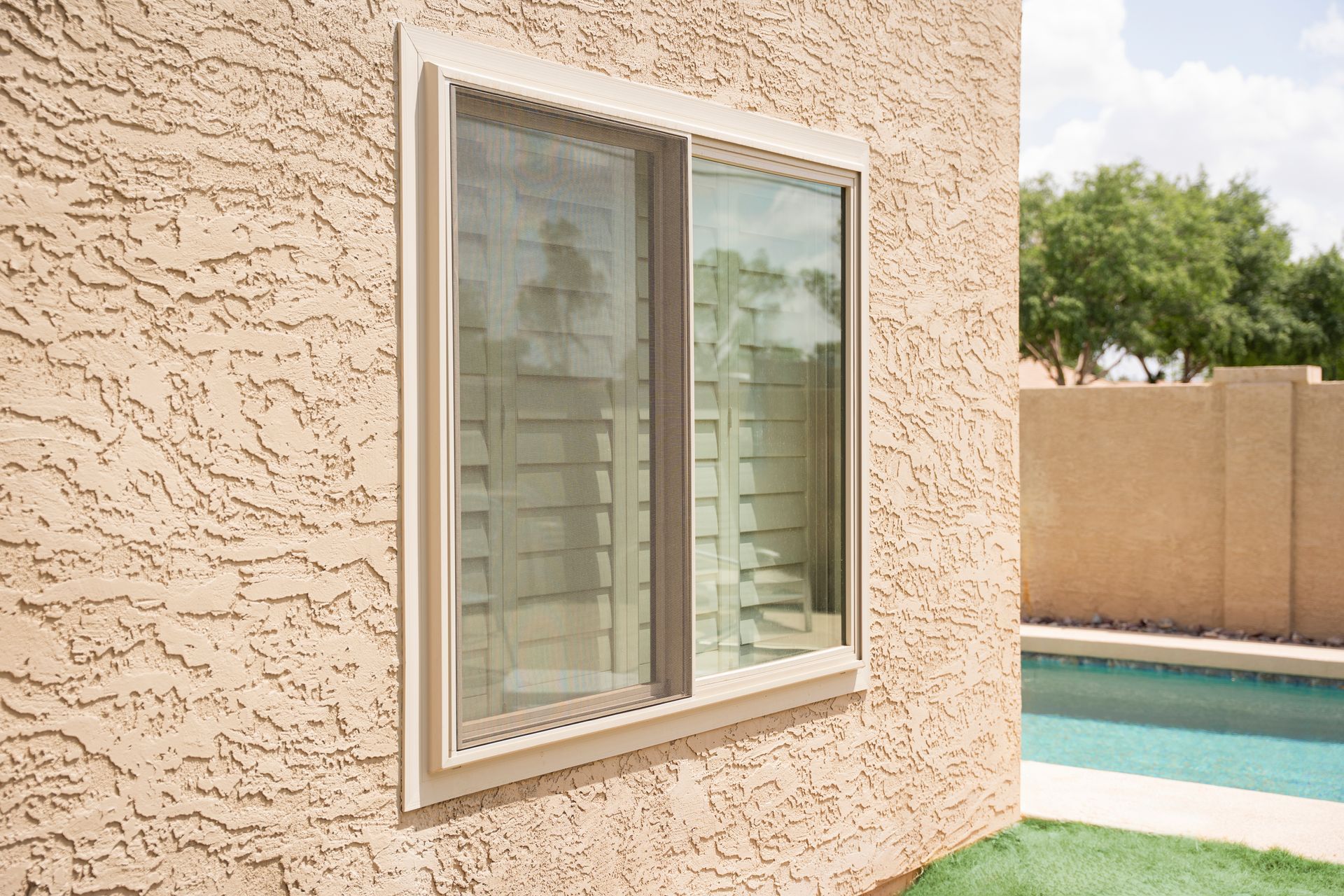 Exterior wall with a window beside a swimming pool and beige privacy fence