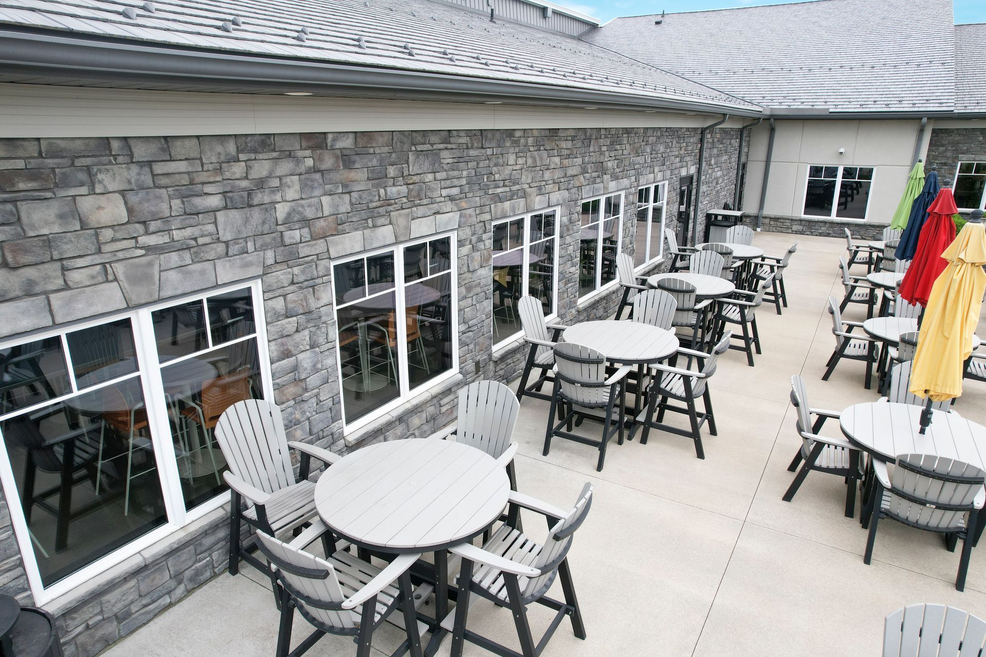 Outdoor patio with round tables, chairs, and colorful umbrellas beside a stone building Outdoor patio with round tables, chairs, and colorful umbrellas beside a stone building