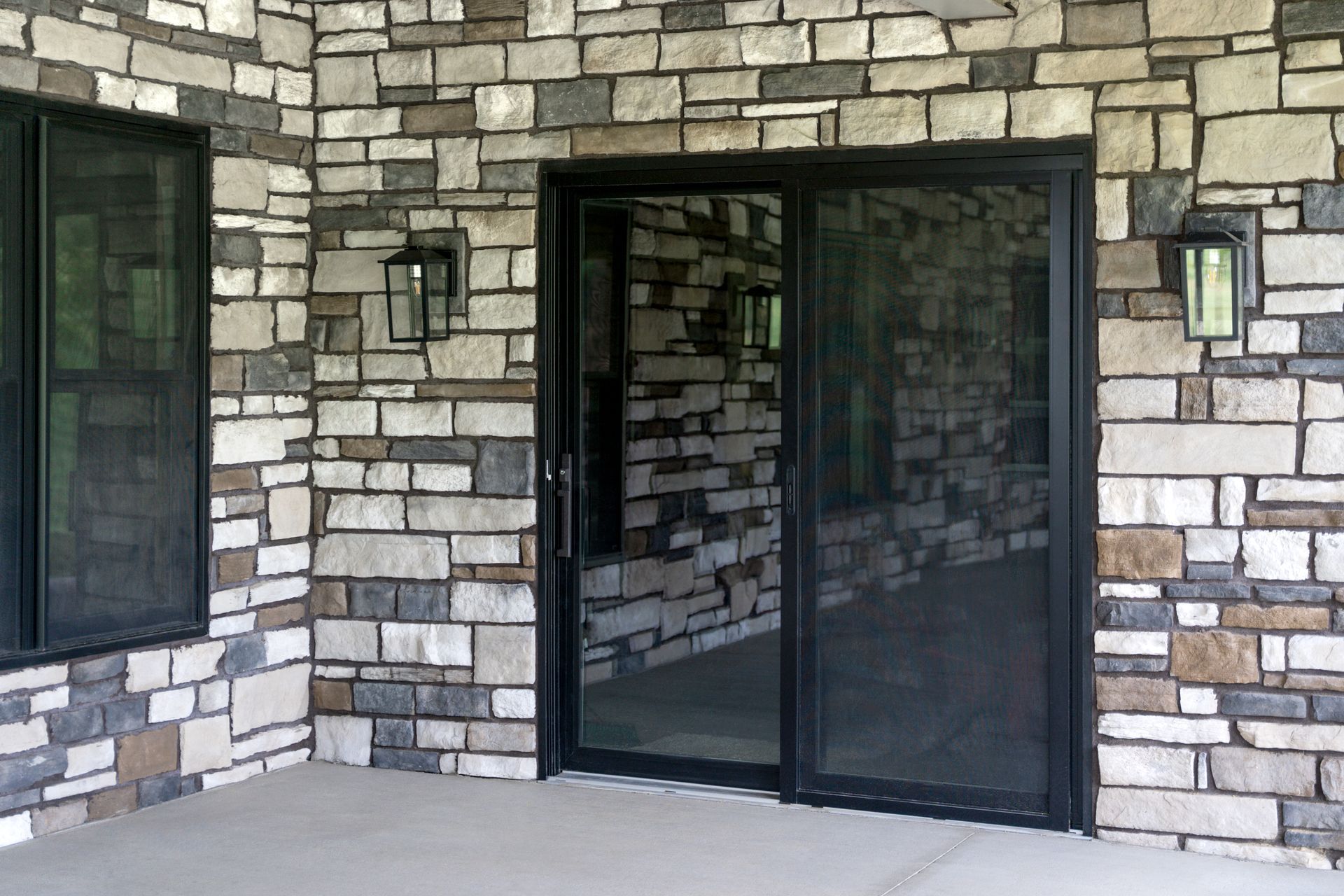 Stone exterior wall with dark-framed glass double doors and windows on a porch Stone exterior wall with dark-framed glass double doors and windows on a porch