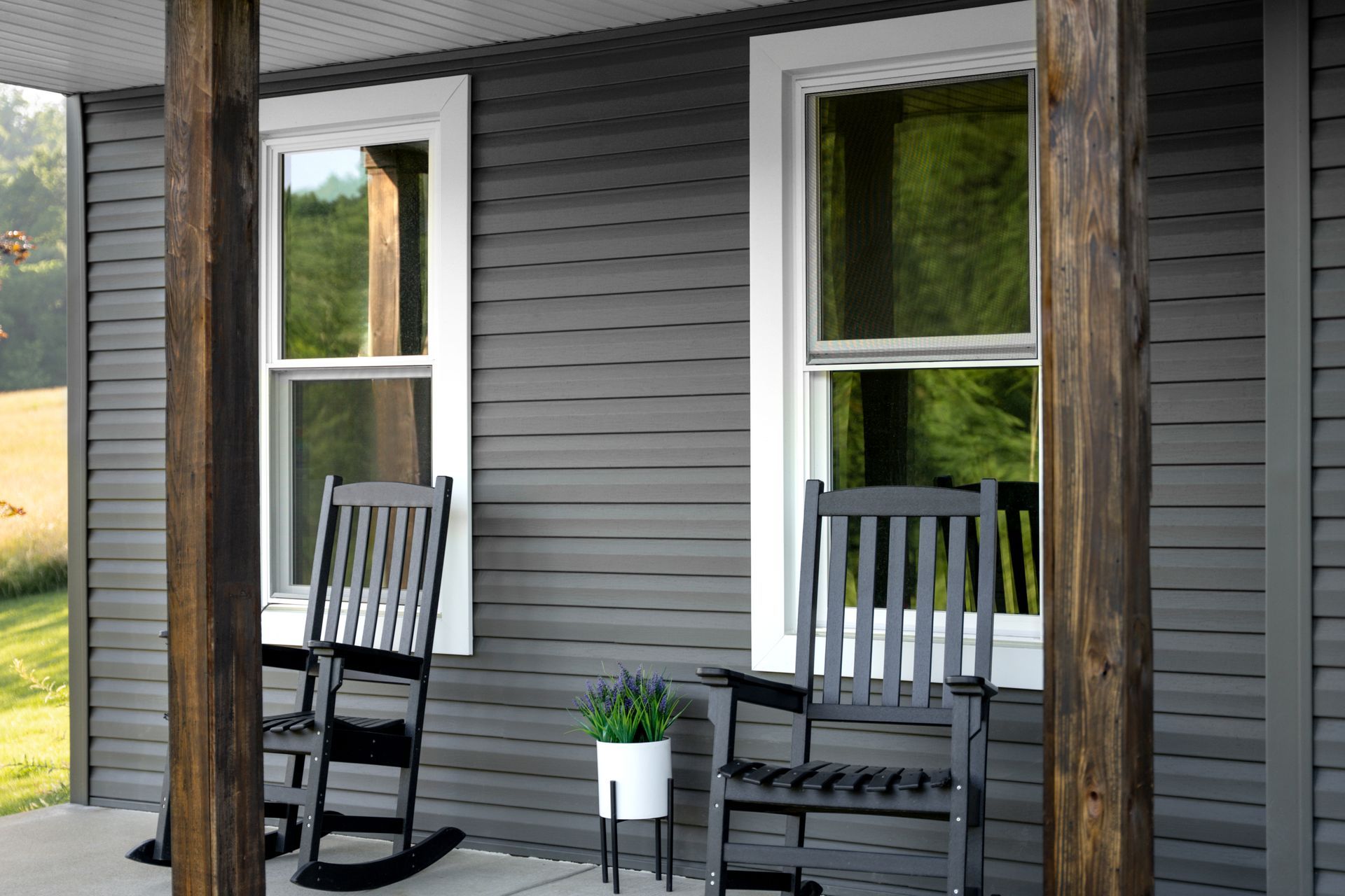 Porch with two black rocking chairs, a small potted plant, and gray siding beside windows