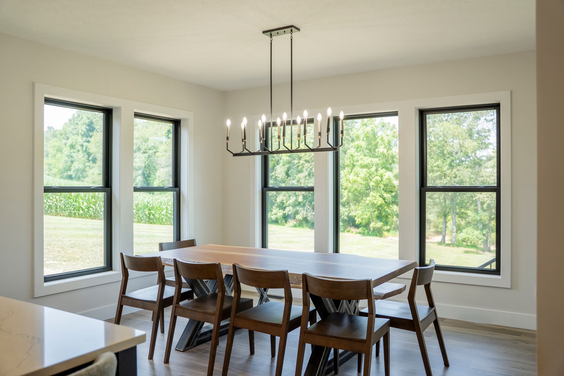 Bright dining room with a long table, wooden chairs, and large windows overlooking greenery Bright dining room with a long table, wooden chairs, and large windows overlooking greenery