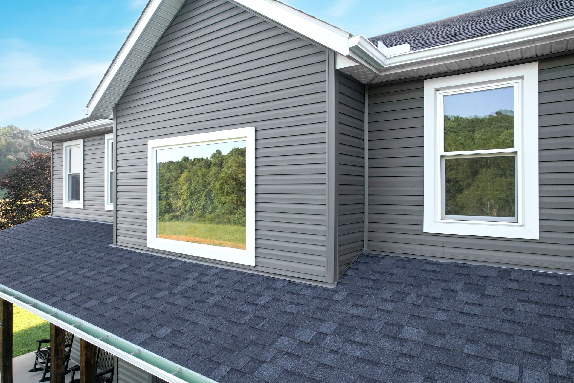 Gray house exterior with shingled roof and white-trimmed windows under a blue sky