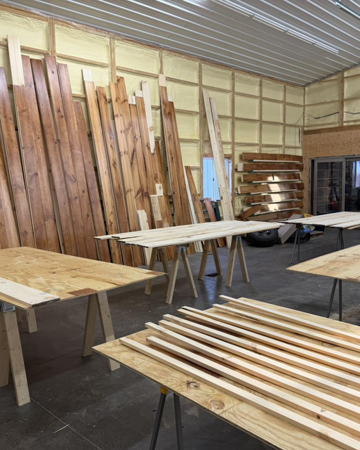 Workshop with stacks of unfinished wooden boards and benches inside a large storage space