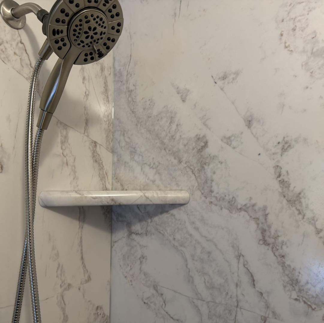 Stainless steel showerhead and shelf against white and gray marble tile wall