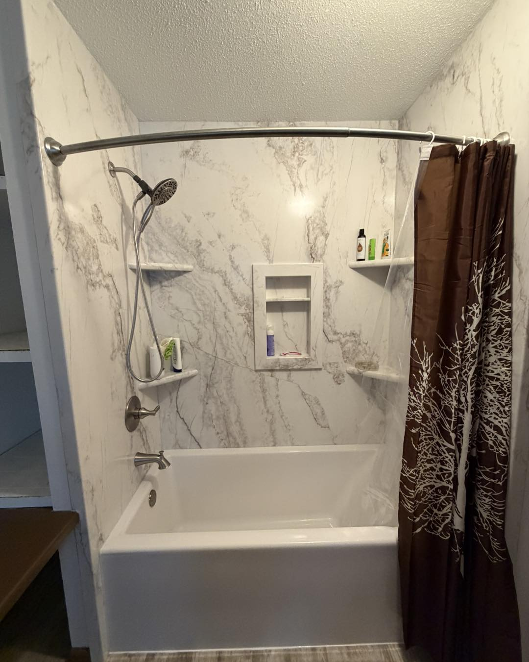 Small bathroom with bathtub, shower curtain, wall shelves, and marble-pattern walls.