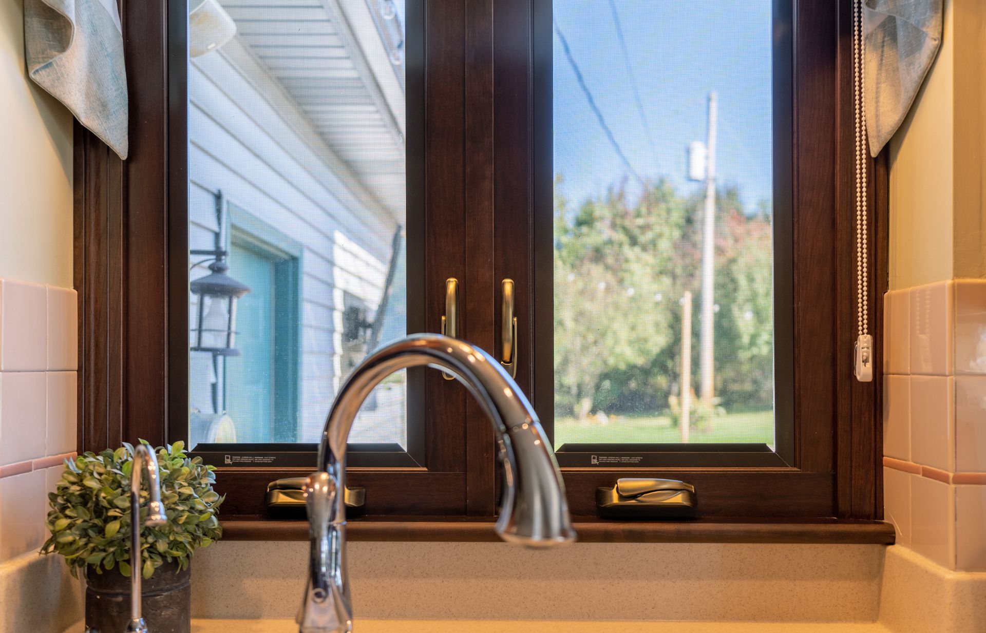 Kitchen sink and faucet below a window looking out onto a bright green yard Kitchen sink and faucet below a window looking out onto a bright green yard