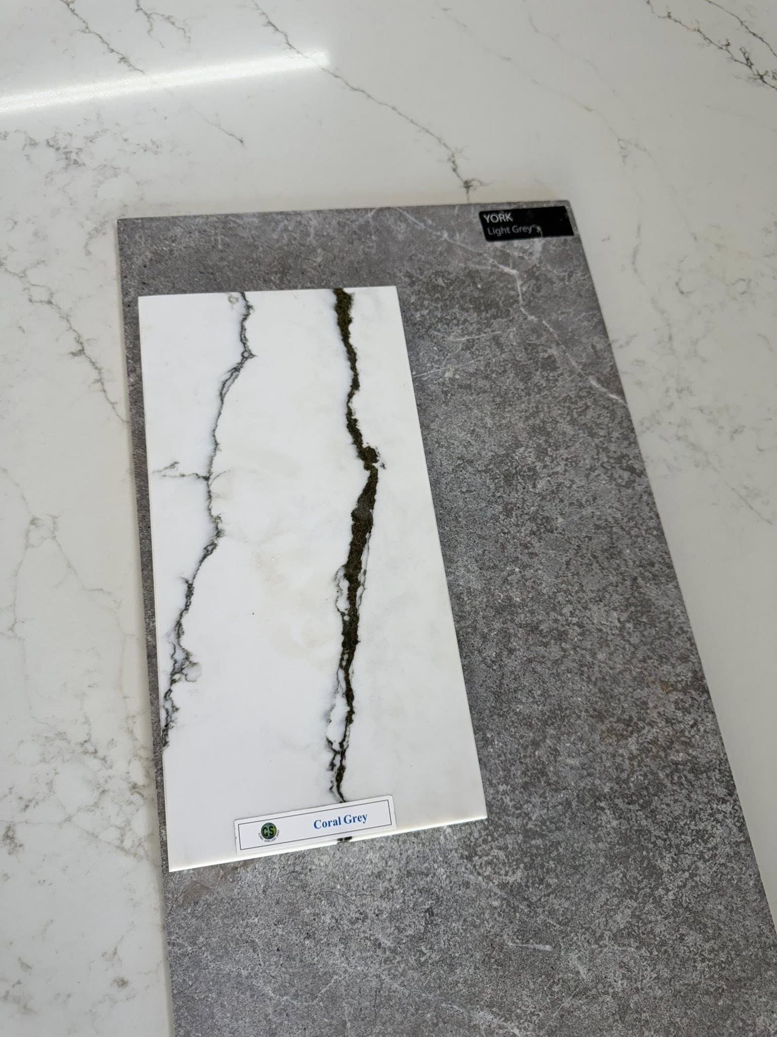 Grey carpet tile with a white marble-like sample showing dark veining cracks.