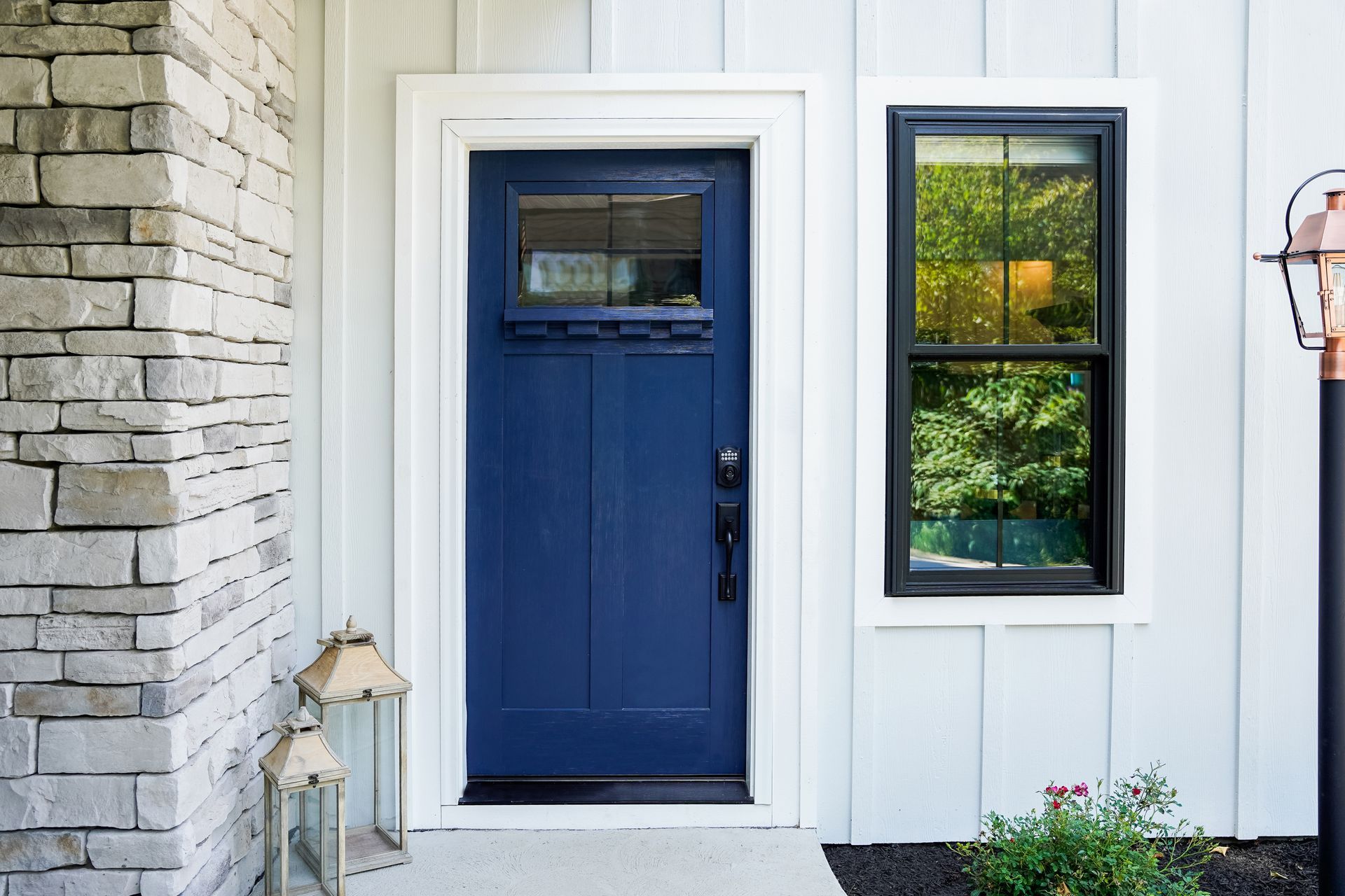 Blue front door with a small window, set in a white siding entryway beside a stone wall. Blue front door with a small window, set in a white siding entryway beside a stone wall.