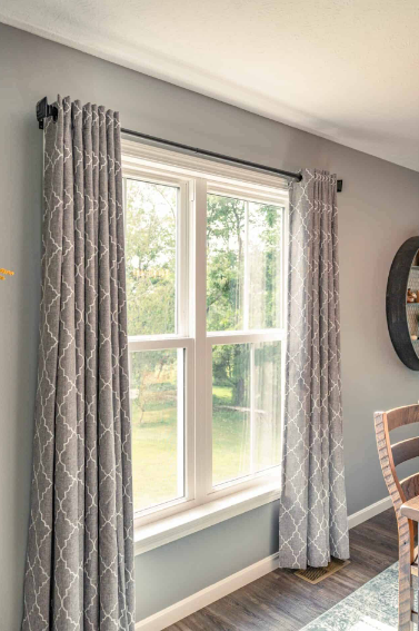 Gray patterned curtains framing a sunlit window in a light gray room with wood floor and dining chair Gray patterned curtains framing a sunlit window in a light gray room with wood floor and dining chair