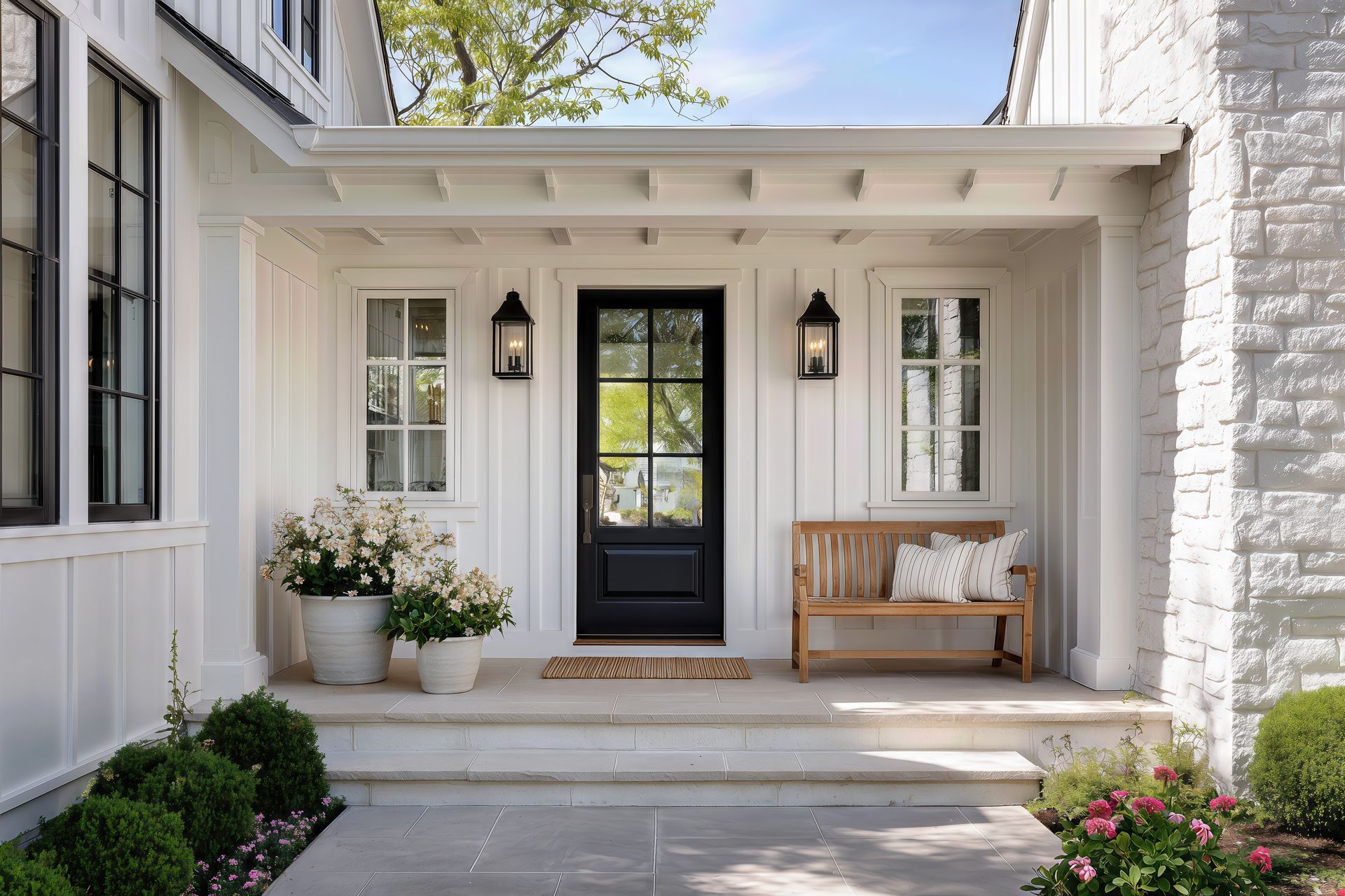 A front door detail of a white modern farmhouse with a black front door, black light fixtures, and decorations under the covered porch