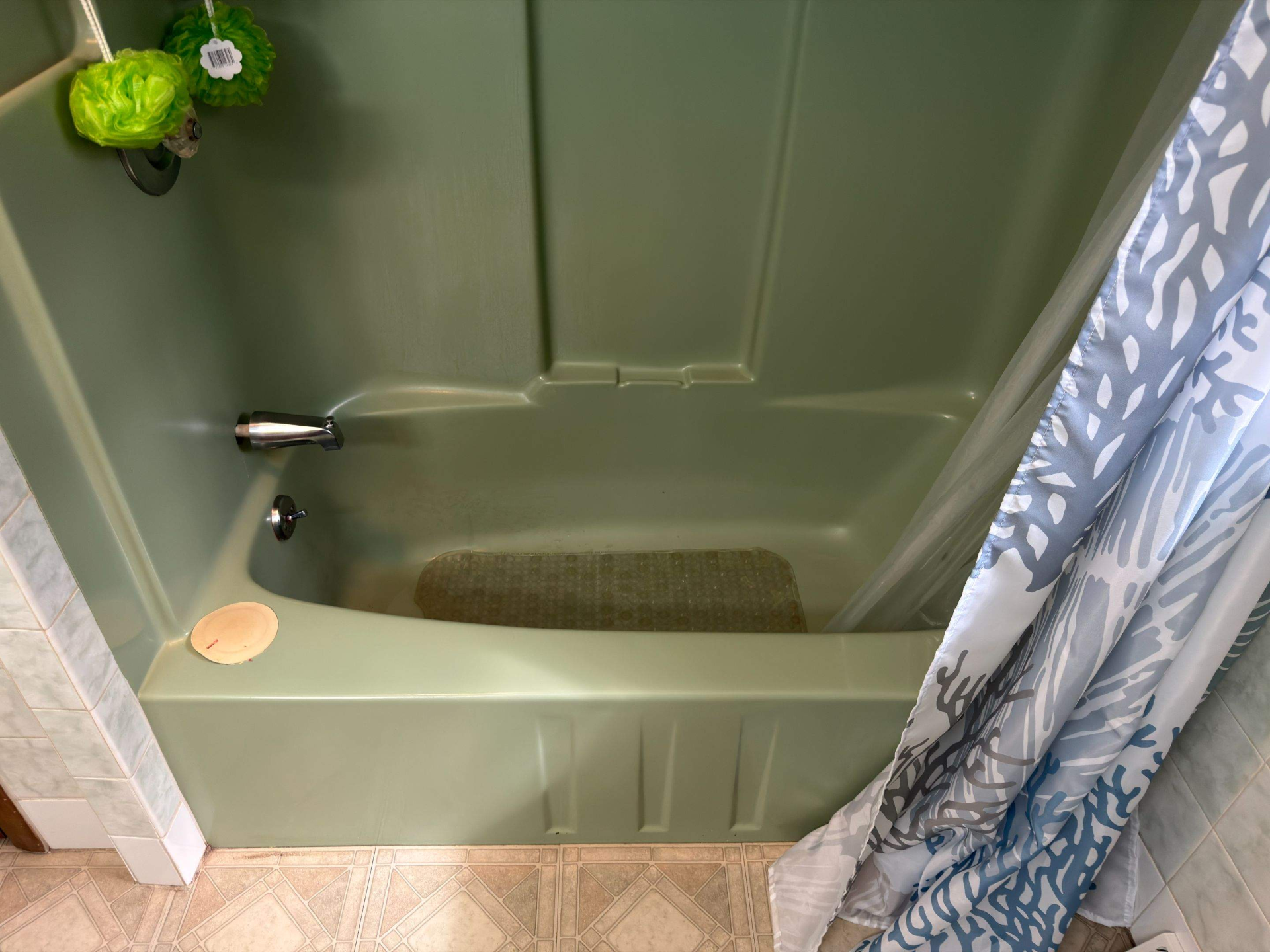 Green bathtub with a shower curtain, soap dish, and towel hanging nearby